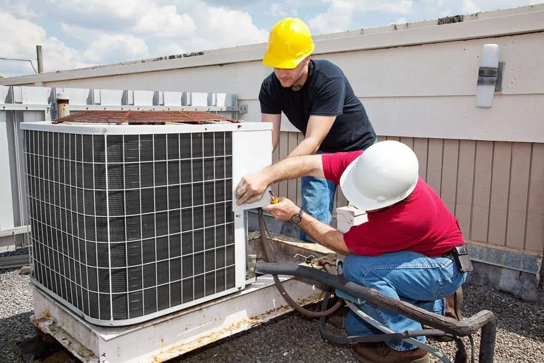 Two men are working on an air conditioner on top of a building.  HVAC installation in Gresham OR