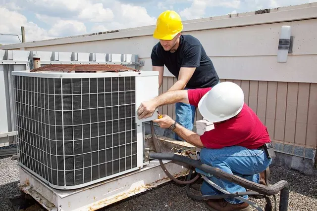 Two men are working on an air conditioner on top of a building.  HVAC installation in Gresham OR